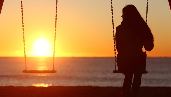 Single woman alone swinging on the beach and looking the other seat missing a boyfriend