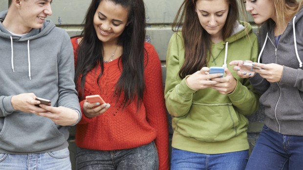 Group Of Teenagers Sharing Text Message On Mobile Phones