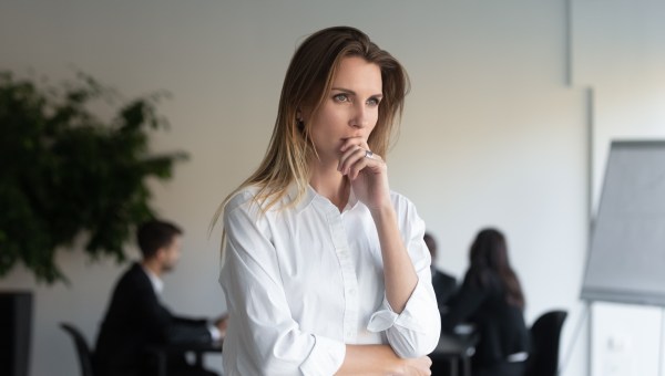 zamyślona kobieta w biurze stoi przed oknem i patrzy przed siebie