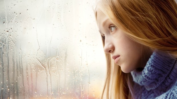 smutna nastolatka siedzi przy oknie i patrzy na krople deszczu na szybie