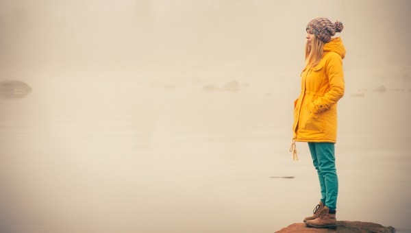 young woman facing water outside on rock