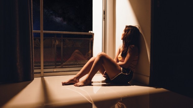 Sad woman sitting on floor looking out window
