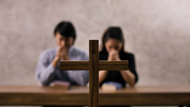 para wiernych modli się w kościele przed krzyżem za kogoś