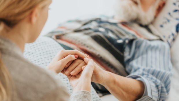 Młoda kobieta trzyma w dłoniach rękę swojego umierającego w szpitalu ojca