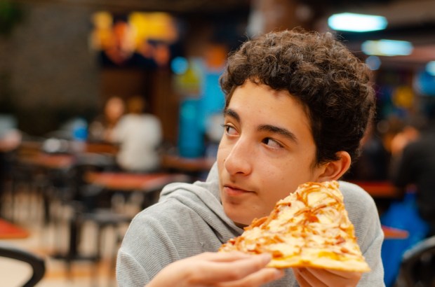 nastolatek je pizzę ze znajomymi w pizzerii i słucha ich rozmowy