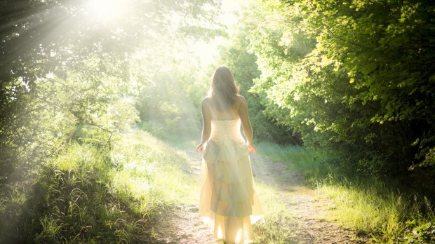 Piękna młoda kobieta w eleganckiej białej sukni idzie drogą w promieniach słońca