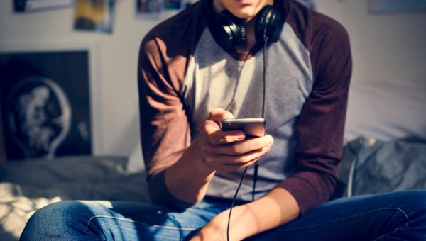 Teenage boy in a bedroom listening to music through his smartphone