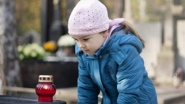 Dziewczynka wpatruje się w znicz, który postawiła na nagrobku