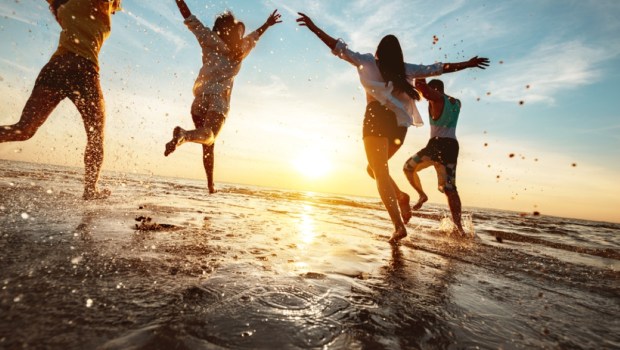 Four happy friends at sunset beach party runs to water