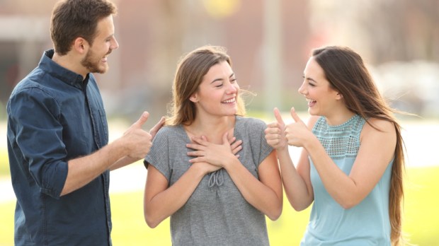 Two friends congratulating a happy girl standing in the street