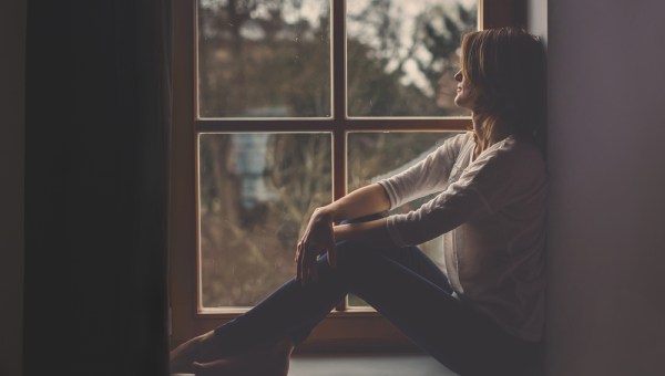 Young attractive woman, sitting on a window, looking outside, lonely mood