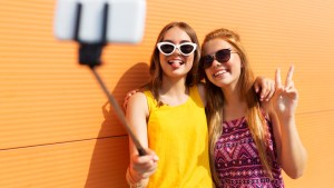 smiling teenage girls taking picture by smartphone on selfie stick
