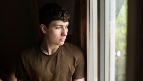 A young teenager boy with sadness in his eyes looks out the window