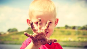 Child little blonde boy kid playing outdoor showing dirty muddy hands