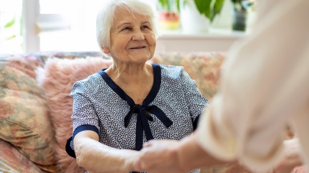 An elderly woman smiling at a person holding their hands