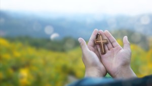 man praying with cross in nature sunrise background