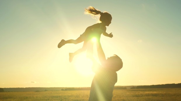 Dad tosses a happy child up into the sky at sunset