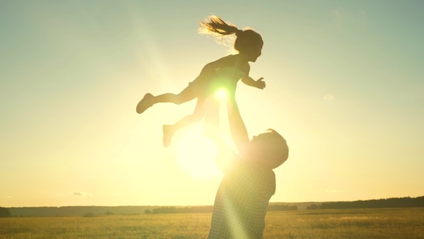 Dad tosses a happy child up into the sky at sunset