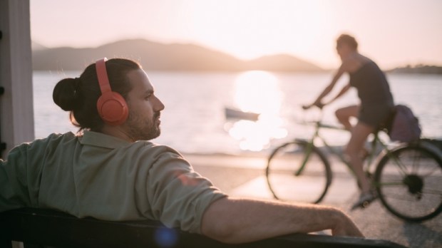 Portrait of a young man in bright large headphones listening to music, audiobook by the sea at sunset