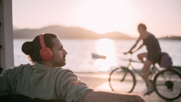 Portrait of a young man in bright large headphones listening to music, audiobook by the sea at sunset
