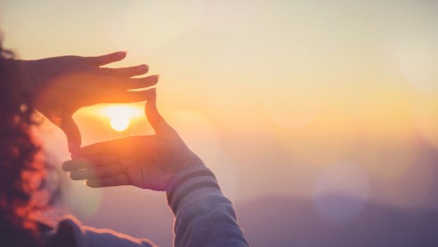 The woman making frame round the sun with her hands in sunrise