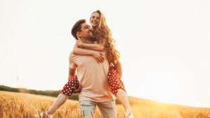 man giving woman piggy back ride looking away standing in the wheat field