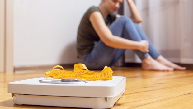 White scale and depression, upset and sad woman with measuring tape on wooden floor