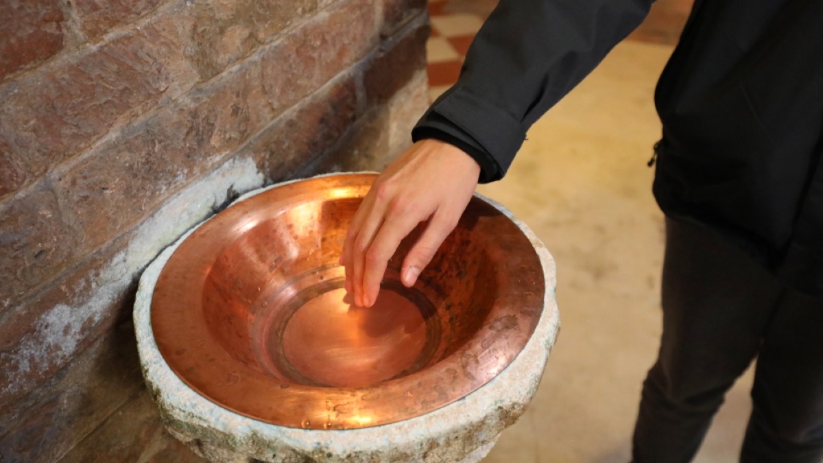 Faithful plunges his hand into the holy water of a Catholic church to make the sign of the cross