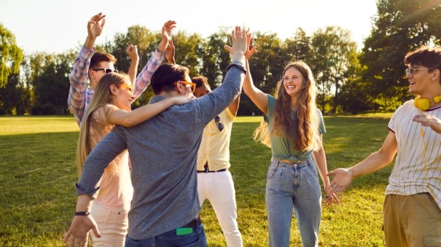Group of happy young people have fun together while walking in park on warm summer evening