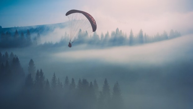 Paraglide silhouette flying over misty mountain valley