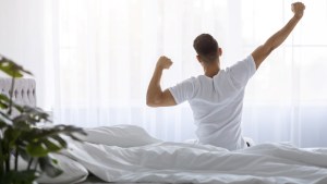 Rear View Of Young Man Stretching In Bed After Waking Up In The Morning