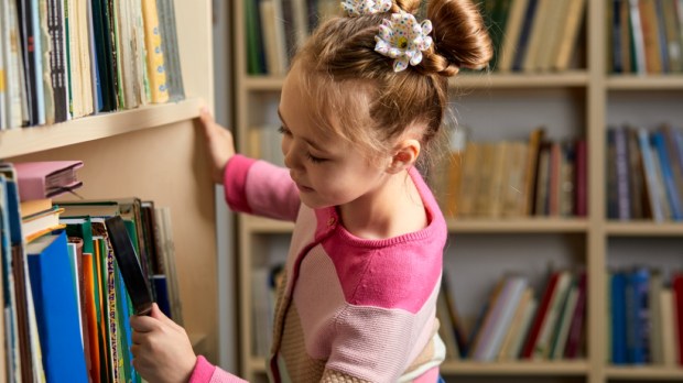 kid girl with ponytails choosing books in library after classes