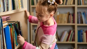 kid girl with ponytails choosing books in library after classes