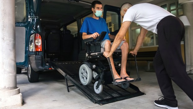 Man on wheelchair using accessible vehicle with ramp for transportation with driver helping.