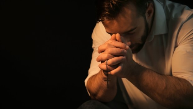 Religious young man praying to God on black background