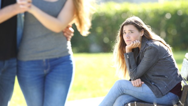 Sad single girl seeing an affectionate couple who are walking outdoors in a park