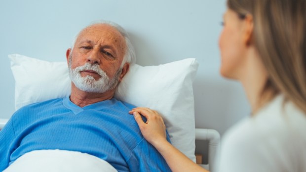 Sick man looking at upset daughter while lying on bed in hospital