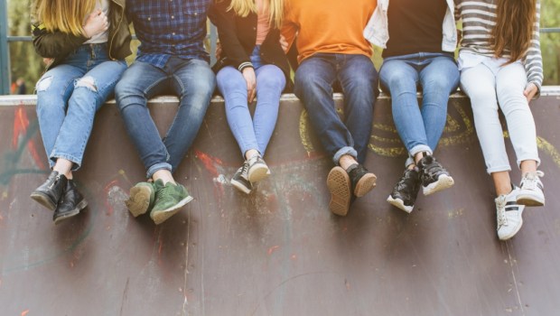 group of smiling teenagers with skateboard hanging out outside