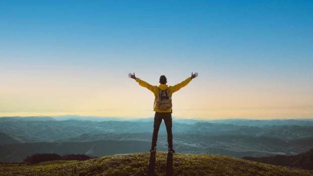 Hiker with arms up standing on the top of the mountain
