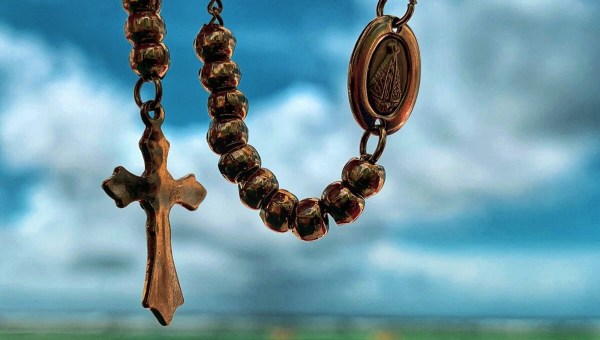 Close up of rosary against a cloudy sky and green grassy background
