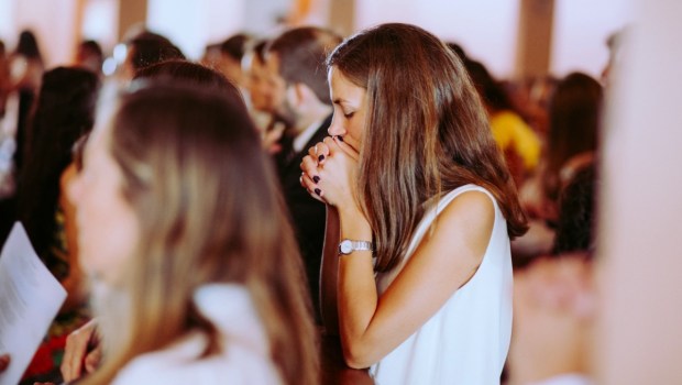 Young woman kneeling in prayer in church with others