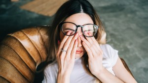 Zmęczona i zaniepokojona kobieta przeciera oczy pod okularami
