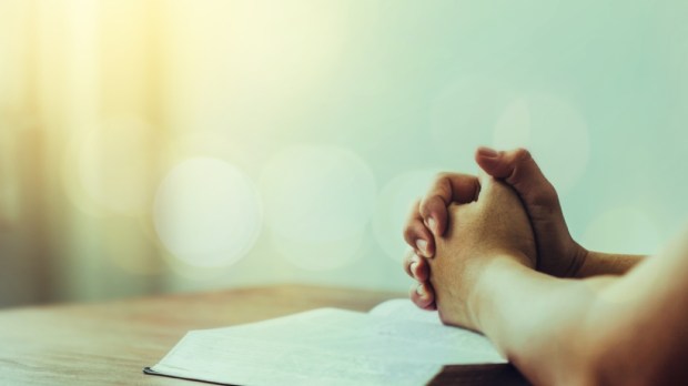 A man praying over bible on wooden table with window and bokeh light, open bible with blurred page, copy space