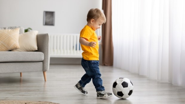 Adorable little toddler boy playing football, hitting ball at home