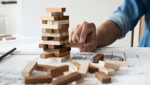 Hand of engineer playing a blocks wood game (jenga) on blueprint or architectural project