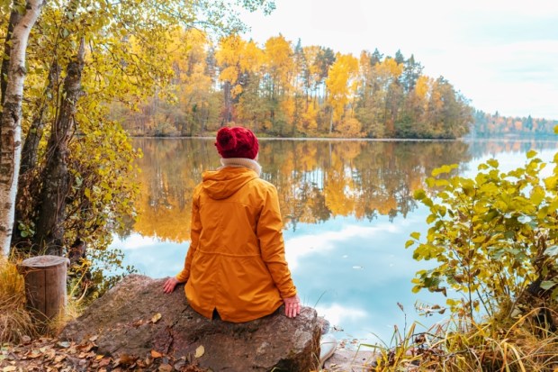 Lonely woman is sitting on the shore of a forest lake