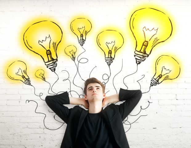 Thoughtful young man with light bulbs on brick background
