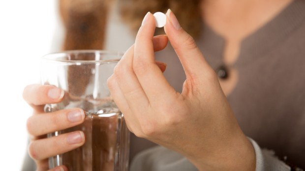 female hands holding one white round pill and glass of water