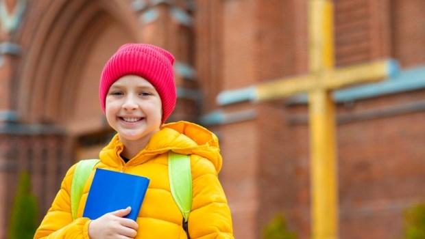 smiling happy child in a hat and jacket, holds a children's bible in his hands, goes to Sunday school