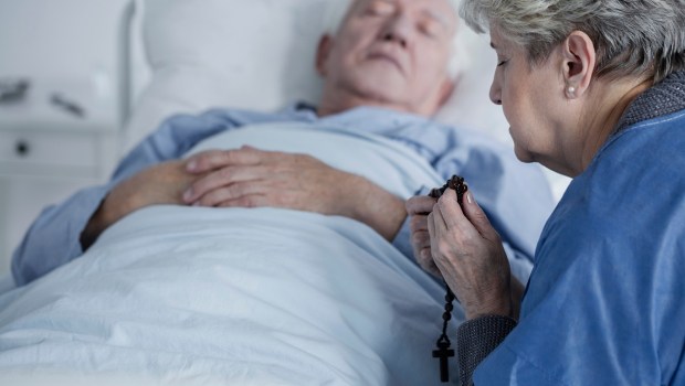 woman praying over man in sickbed